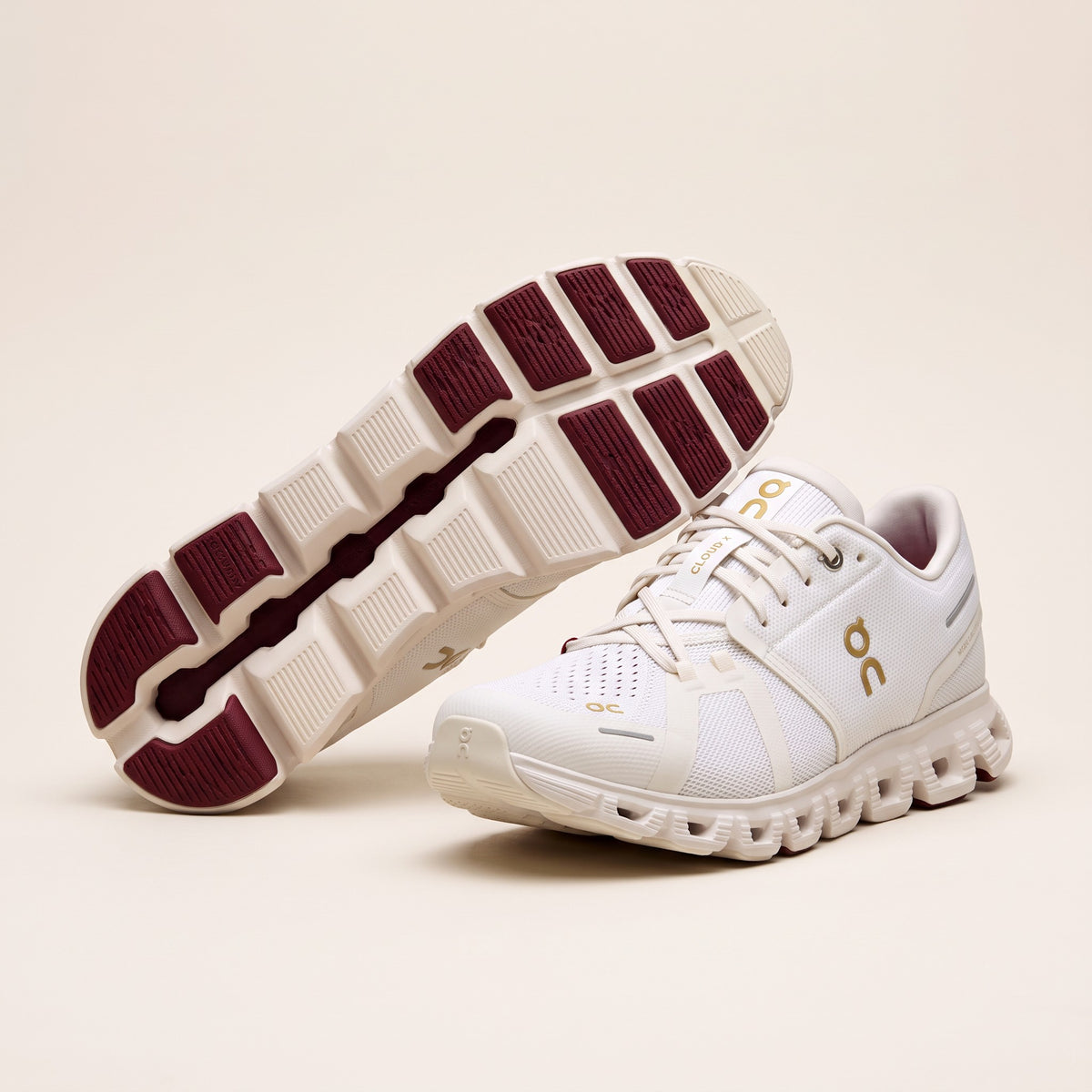 Pair of ivory sneakers, one turned over to show the burgundy outsole